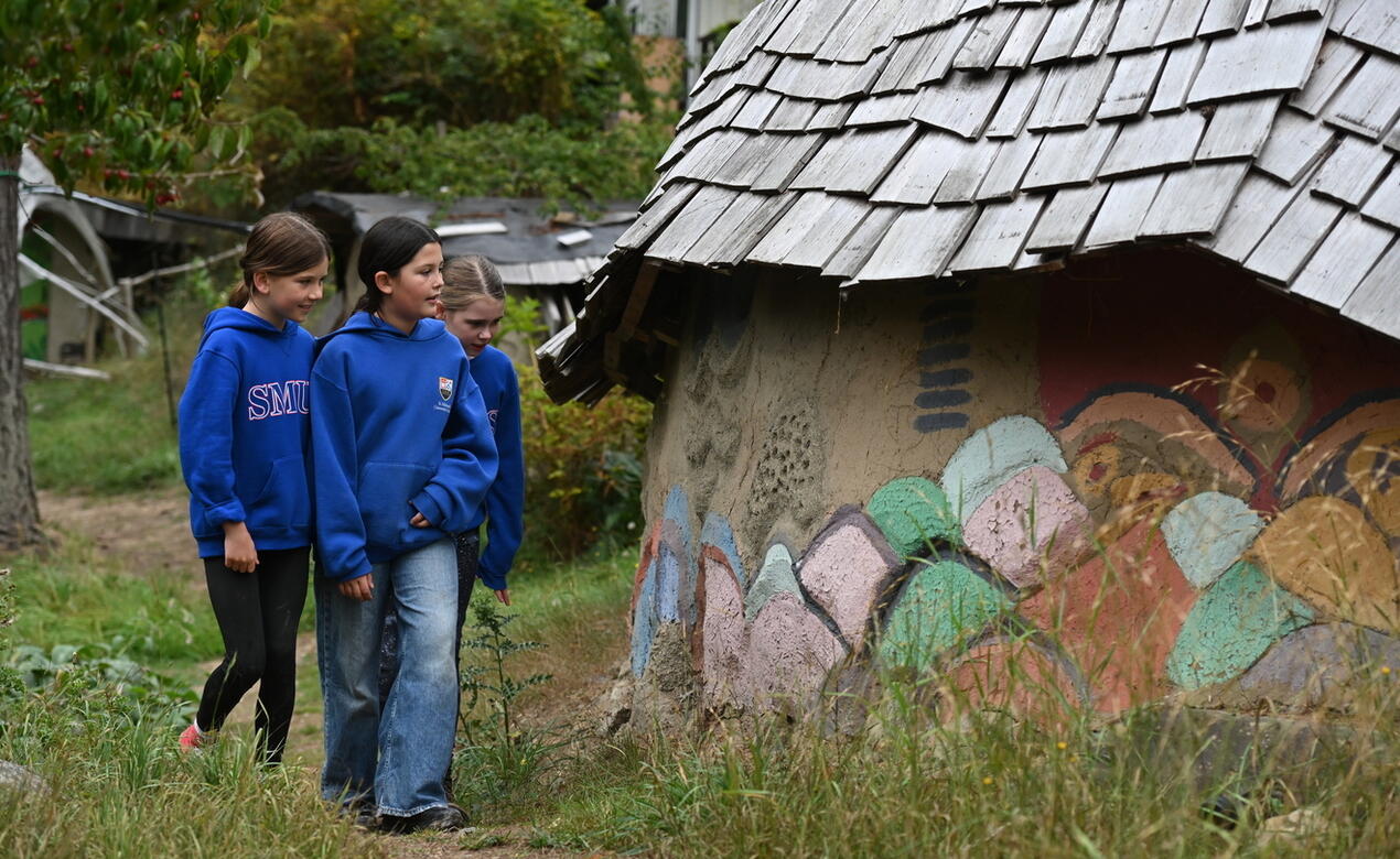 Grade 6 students walk up a path admiring the Ecovillage Dragon Wall with artwork from generations of SMUS students