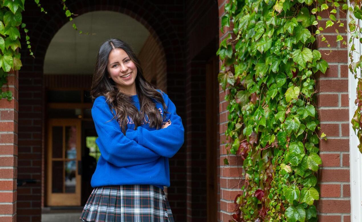 Abi Portriss poses with her arms cross in front of the iconic Crothal building brick arch with ivy creeping down the walls. 