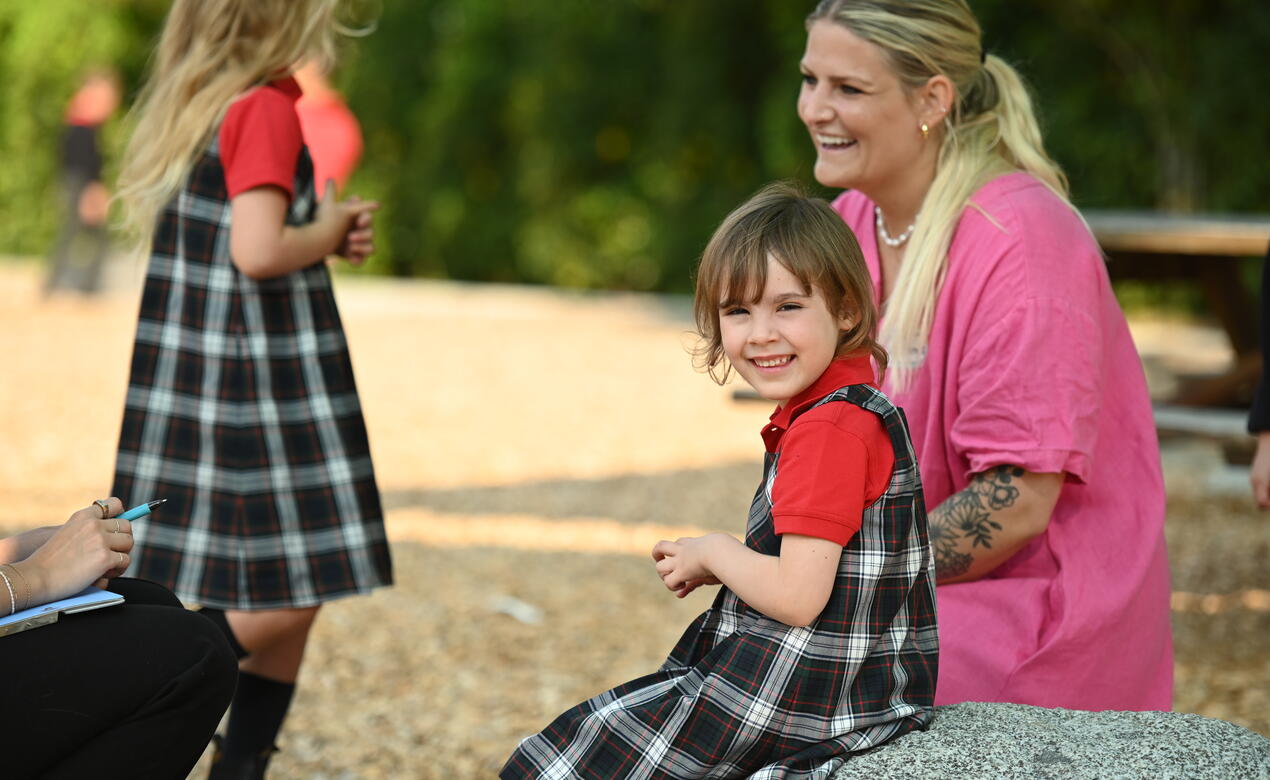 Kindergarten student smiles with teacher Ms. Barnes in the background