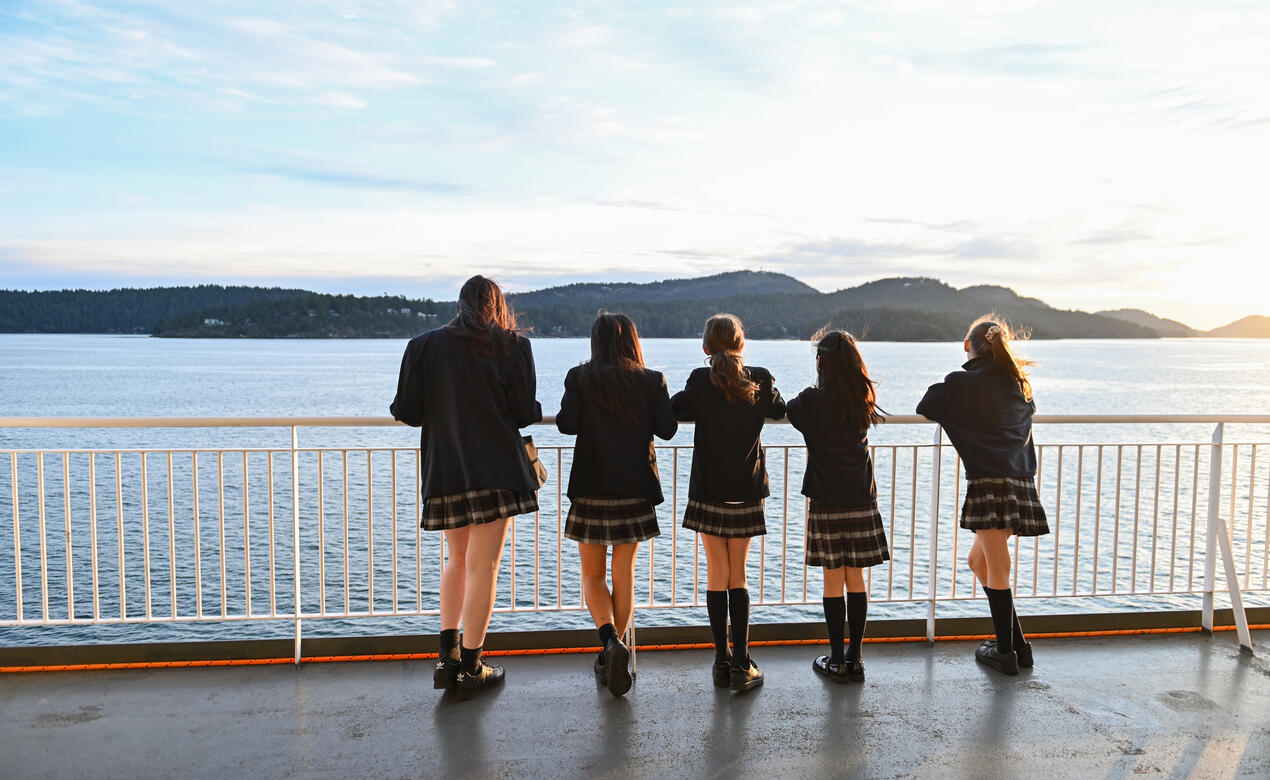 Five middle school students stand on the balcony of the BC Ferries looking out over the ocean as the sun rises.