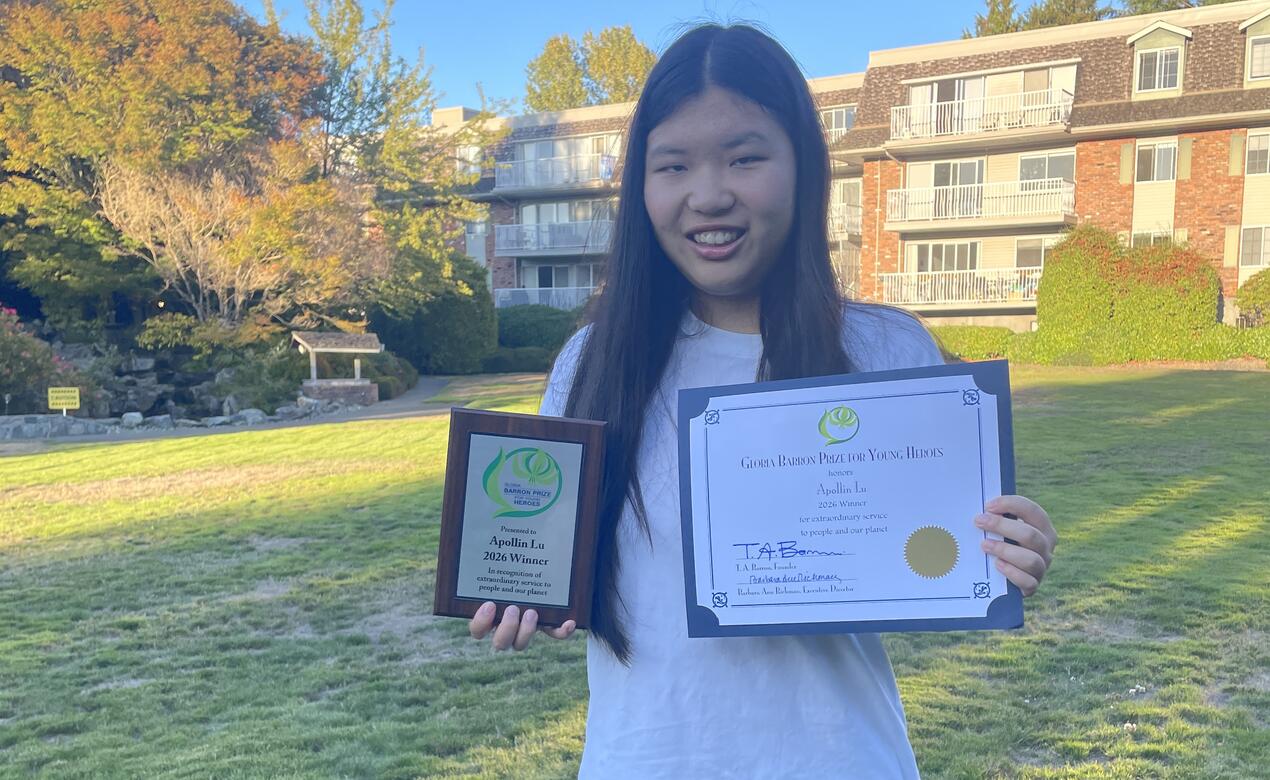 Apollin Lu poses outside holding her certificate and plaque as a Gloria Barron award winner. 
