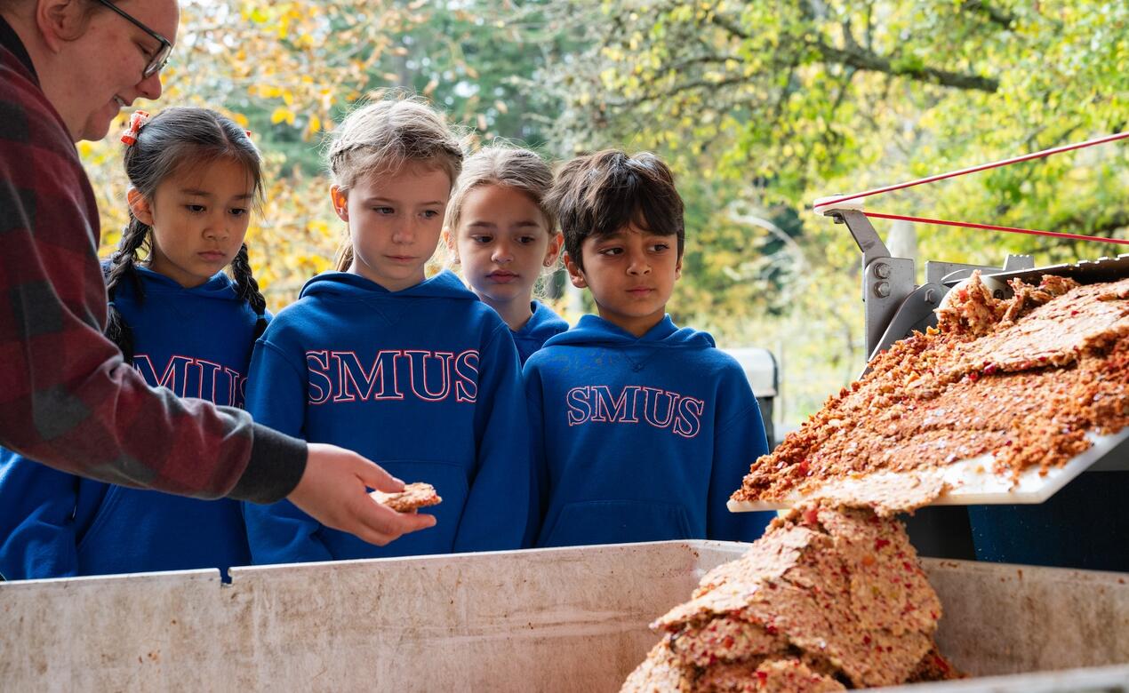 Four students look on as apples are pressed through a machine to make fruit leather. 