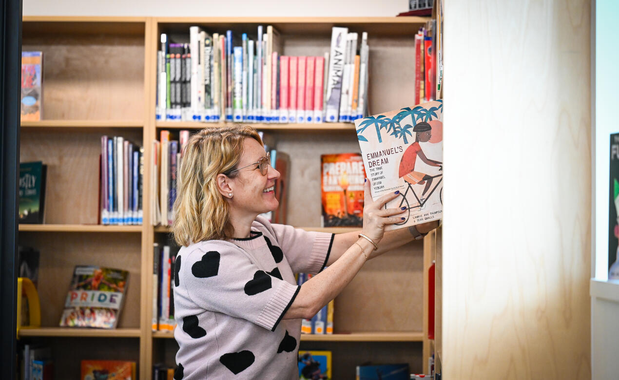 Sarah Bailey, Middle School Librarian, smiles while placing Emmanuel’s Dream on a library shelf.