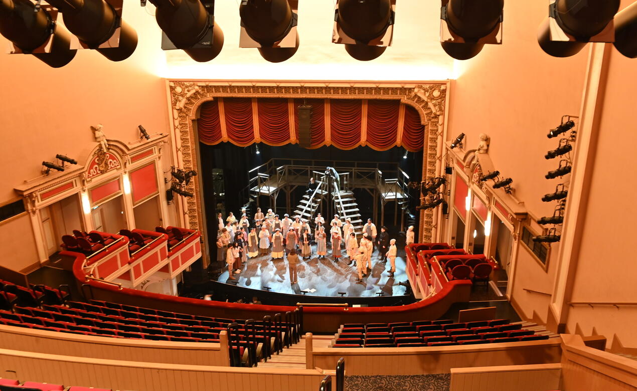 A wide shot of the McPherson Playhouse with students rehearsing on stage. 