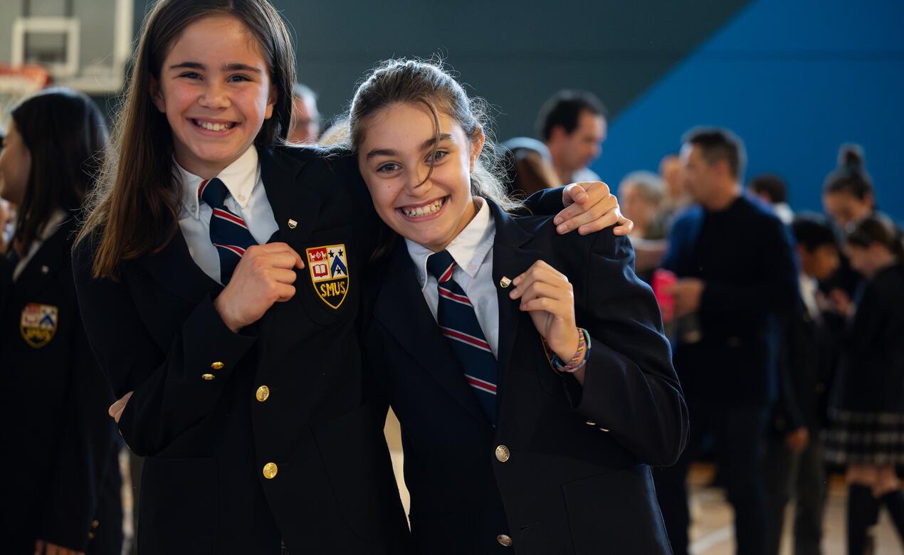 Two Grade 5 students show off their new leadership pins on their blazer, smiling at the camera. 