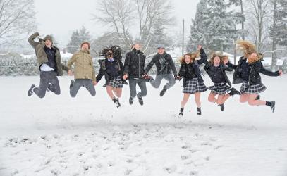 A group of Senior School friends holding hands and jumping in snow