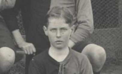 An archival photo of a young boy with his arms crossed in front of him.