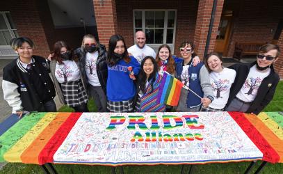 Students stand in front of a colourful Pride Alliance banner