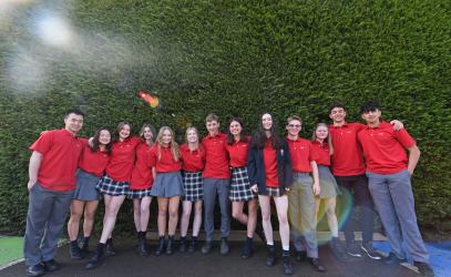 A group of Grade 12 Lifers stand in front of a hedge at the Junior School in red polos and pose for a photo.