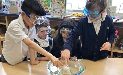 Grade 1 students conduct a science experiment using a bowl of water, a cup and a piece of scrunched paper towel.