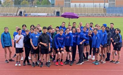 A large group of Middle School students stands on the race track at UVic, smiling for a photo.