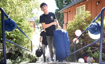 A Harvey House student carries a suitcase up the front steps of the boarding house