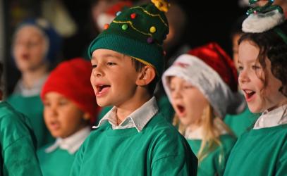 Students wearing winter and Christmas-themed clothing sing on stage at the Junior School