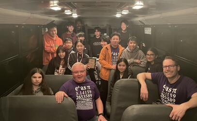 A group of students and their two teachers pose for a group photo from the inside of a bus.