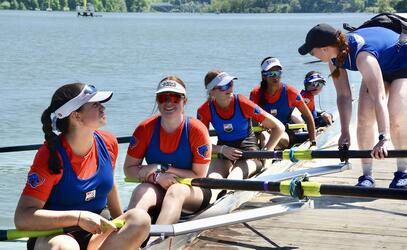 SMUS coxless four women sit in their boat talking to a coach as they prepare for a race.