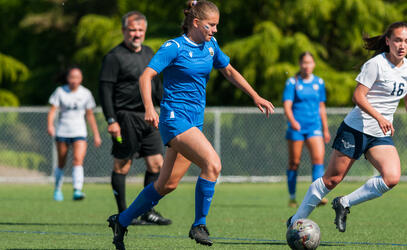 Senior girls soccer player dribbles up the field past an opponent