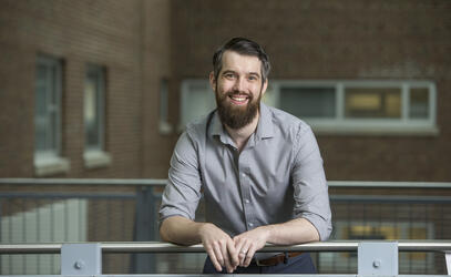 Alumni Dr. Trefor Bazett smiles at the camera while leaning over a railing.