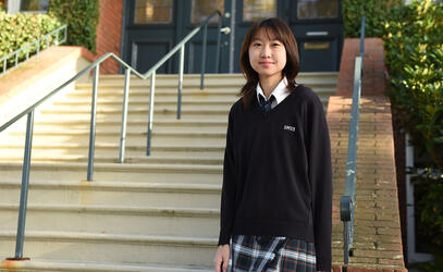 Senior School student Tina Wang '25 stands in front of steps at school house