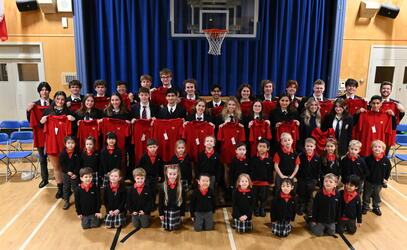 A large class of Grade 12 Lifers poses holding their red shirts up with the current Kindergarten class in front of them. 