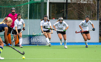 Four SMUS players wearing safety helmets run out from goal to defend a penalty shot