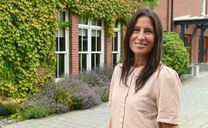 A portrait of Denise Rees near a brick building with ivy