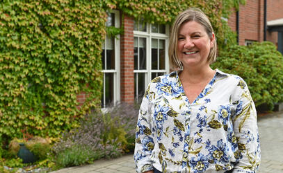 A portrait of Janine Cowie near a brick building with ivy