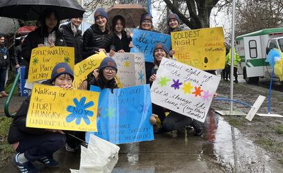 SMUS students brave the rain and hold up their Coldest Night of the Year posters ahead of their 5-km walk