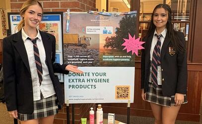 Ruby and Olivia pose with Soap for Hope poster in the lobby of the School House Building