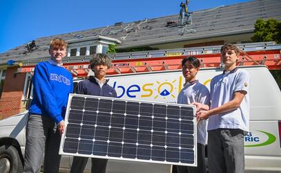 Four Econ 12 students hold up a solar panel that will be installed on the roof of brown hall.