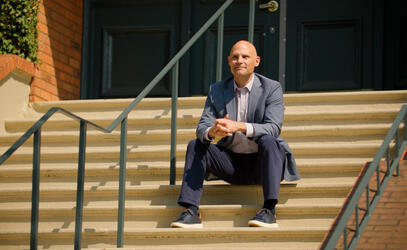Jeff Aitken sits on the steps of School House Building looking out.