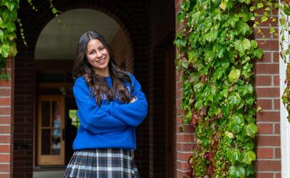 Abi Portriss poses with her arms cross in front of the iconic Crothal building brick arch with ivy creeping down the walls. 