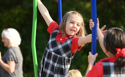 Kindergarten student Maeve reaches for a bar on the playround. 