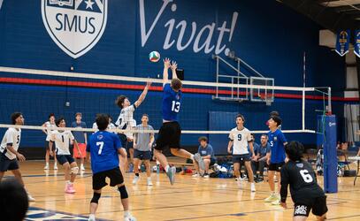 Wide action shot of the Senior Boys volleyball team going up for a block.
