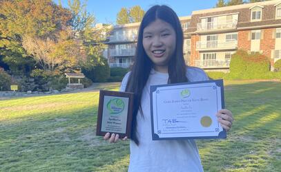 Apollin Lu poses outside holding her certificate and plaque as a Gloria Barron award winner. 
