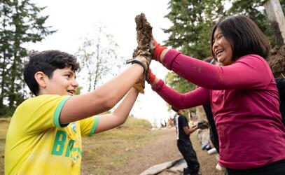 Two students with muddy hands high five each other 