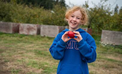 Addie Lee holds up an apple with two hands while at the Sea Cider Apple Farm