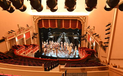 A wide shot of the McPherson Playhouse with students rehearsing on stage. 