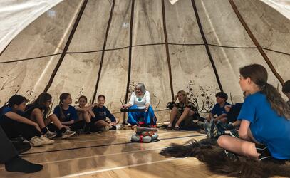 Elder Jo-Ina Young under a large tee pee teaching middle school students