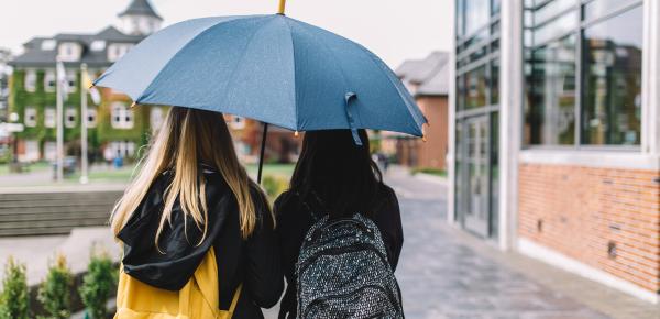 Two students walking through campus under an umbrella