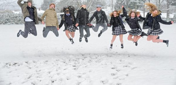 A group of Senior School friends holding hands and jumping in snow