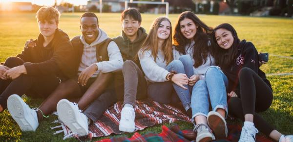 Group of happy Senior School students sitting on a blanket in the field