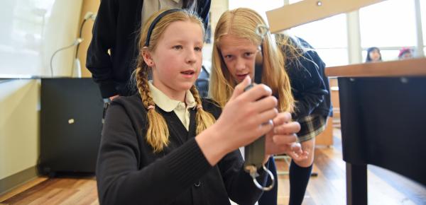 Grade 5 students inspect a weighted lever as part of a simple machine science lesson.