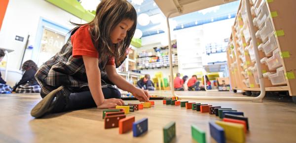 A Kindergarten student lines up dominoes while sitting underneath a table in the Imagination Lab.