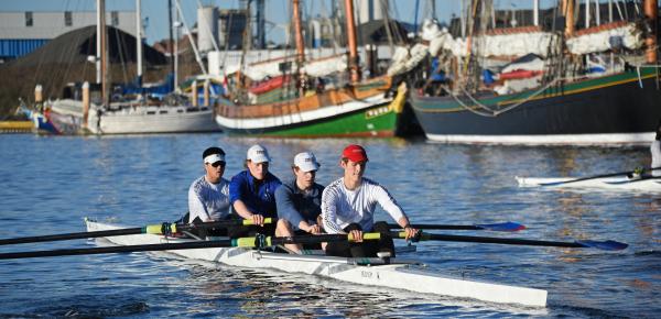 A men's quad rows on the Gorge waterway in front of some boats.