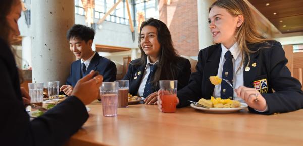 Three Senior School boarding students sit at a table in a dining hall eating a meal.