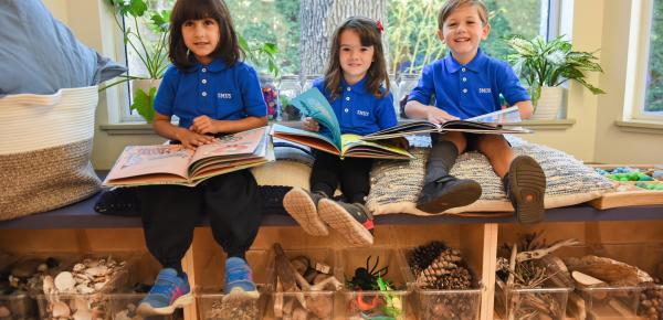 A group of Junior Kindergarten students smile while reading in the classroom