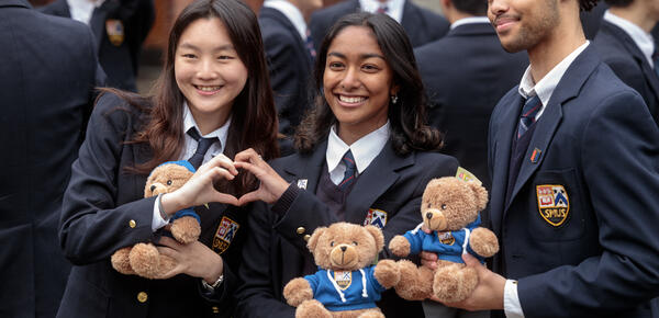 Three Senior School students pose holding their grad teddy bear with two of the female students making a heart together with their hands.