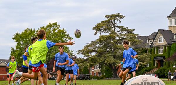 Group of campers playing rugby with a rugby ball in the front of the frame