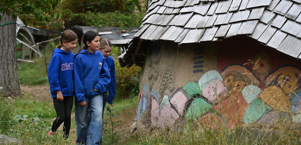 Grade 6 students walk up a path admiring the Ecovillage Dragon Wall with artwork from generations of SMUS students
