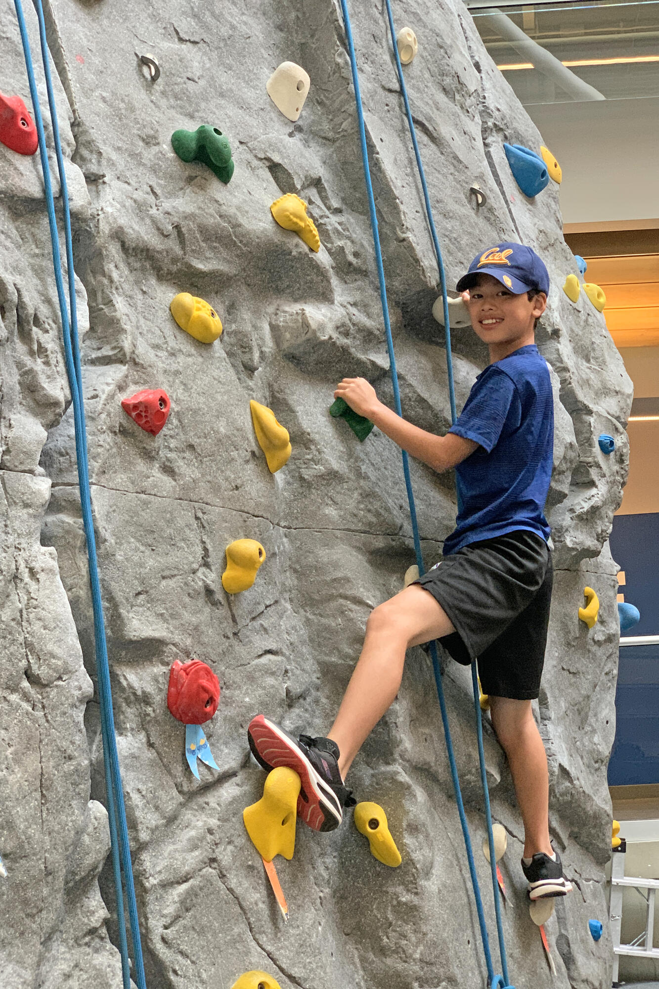 A student smiles for a photo while indoor rock climbing